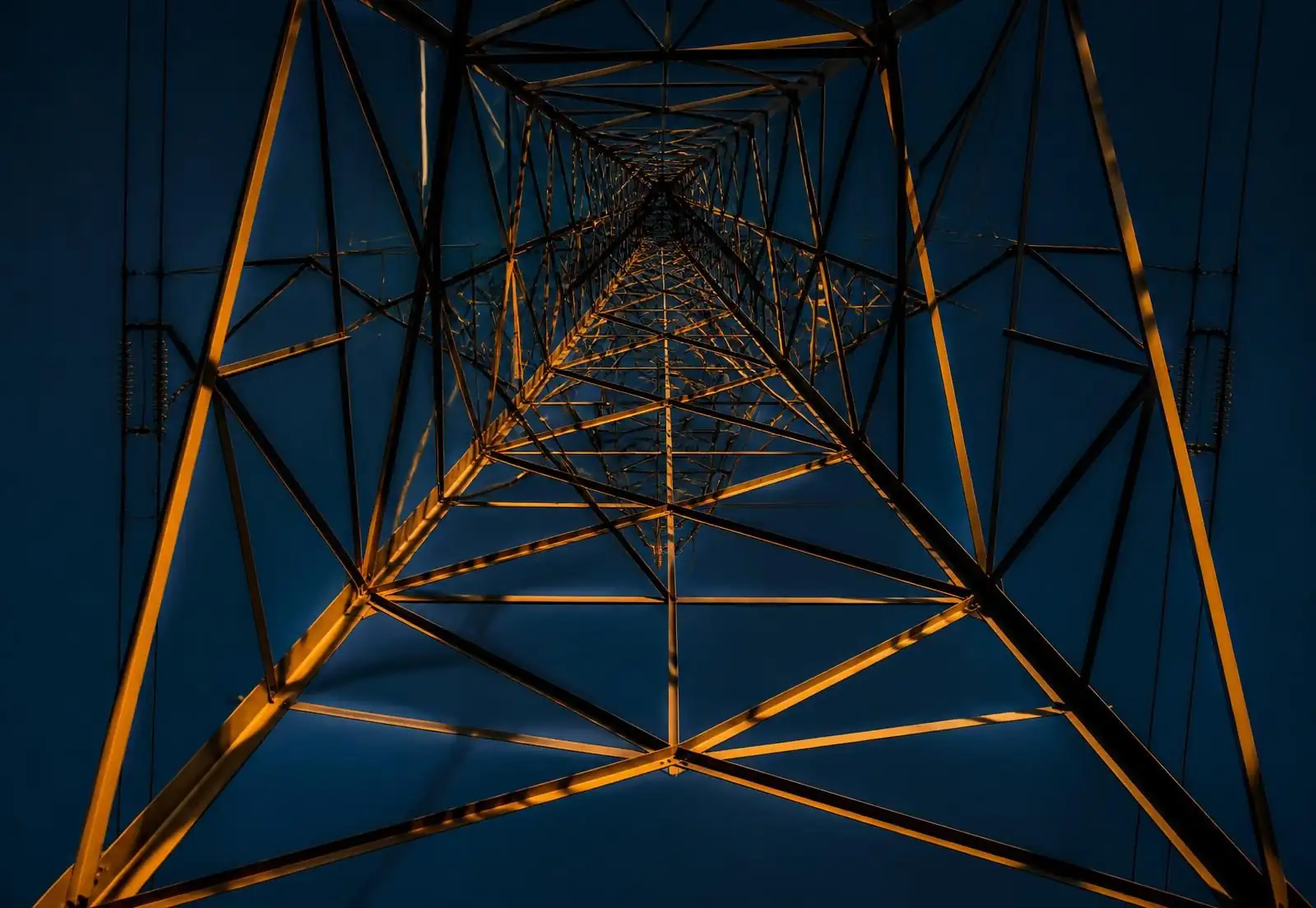 Steel lattice transmission tower photographed from below against a navy sky